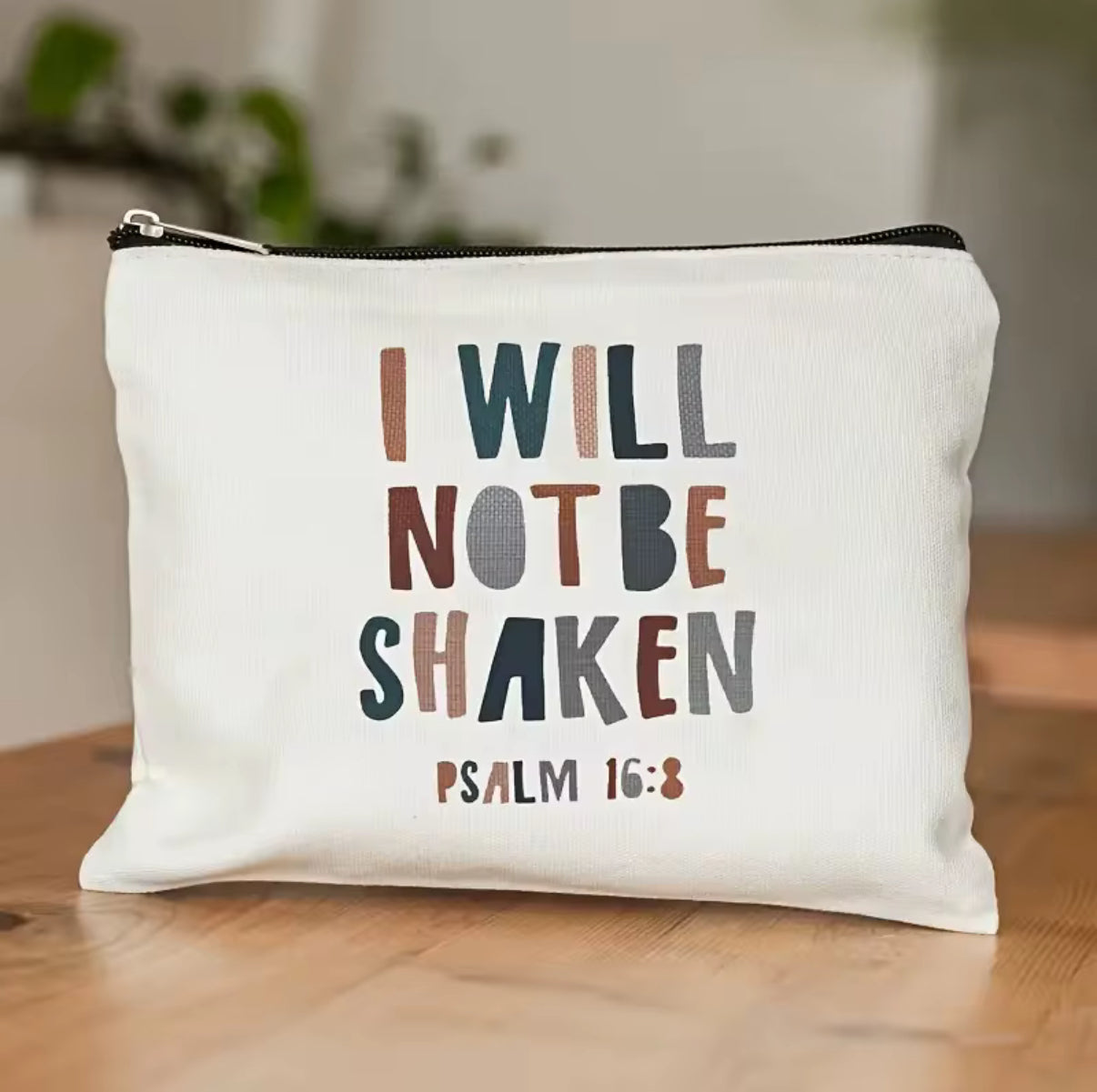 White pouch with motivational quote 'I Will Not Be Shaken' from Psalm 16:8 on a wooden surface.