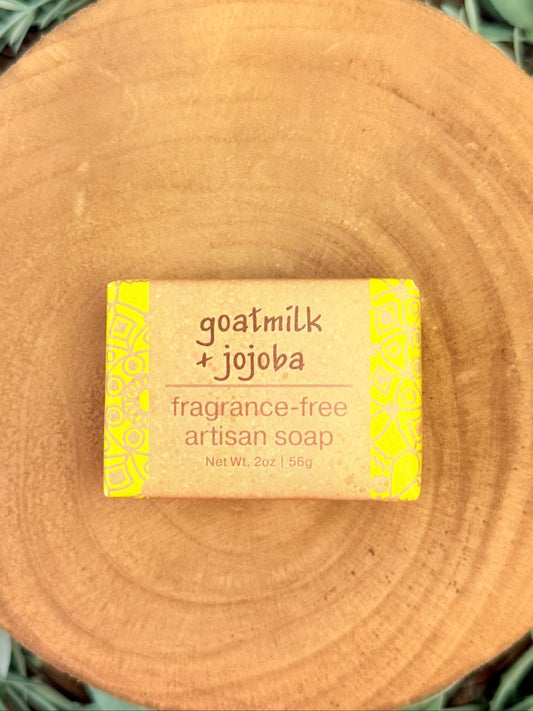 Bar of goatmilk + jojoba soap on a wooden block with a yellow label.